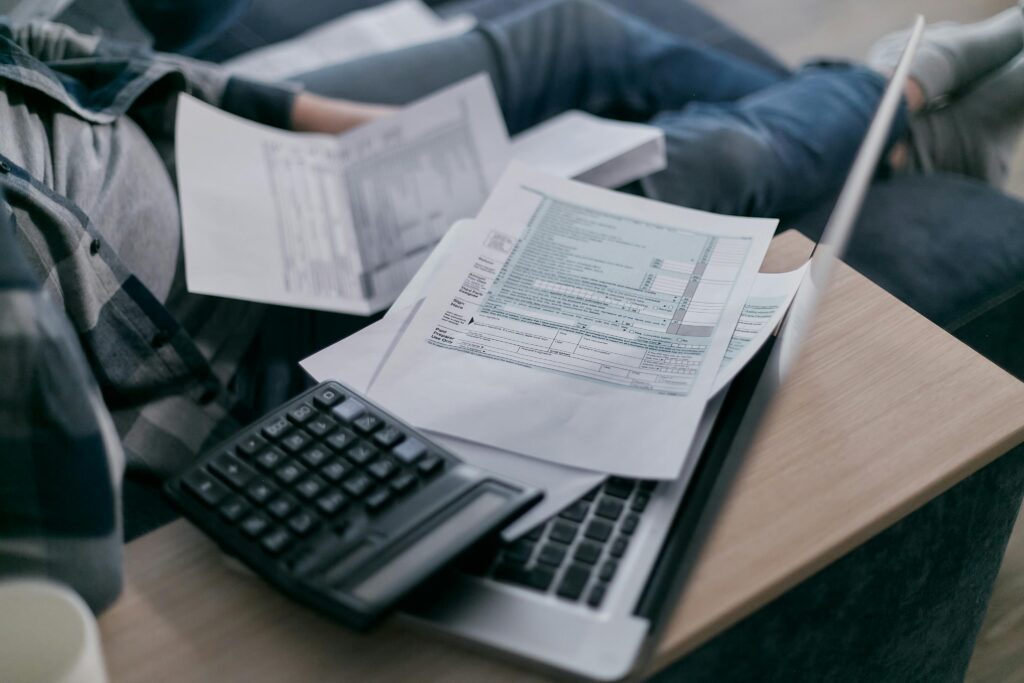 Close-up of a person working with tax documents on a laptop, a calculator nearby. The scene conveys a sense of focus and financial planning.