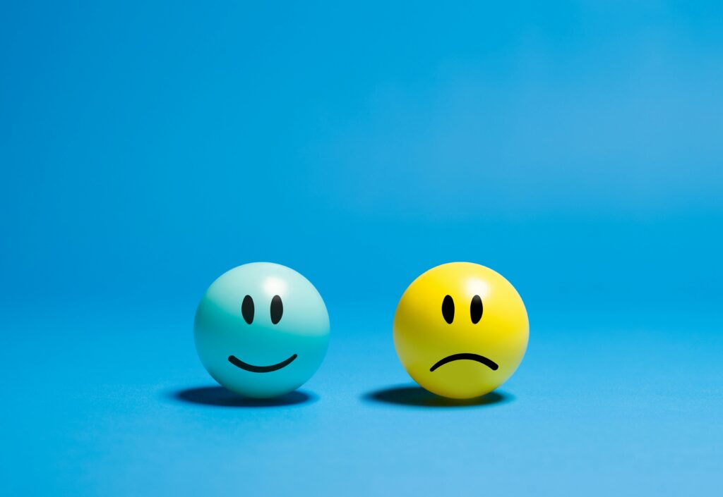 Two balls on a blue background; a light blue ball with a happy face and a yellow ball with a sad face, symbolizing contrasting emotions.