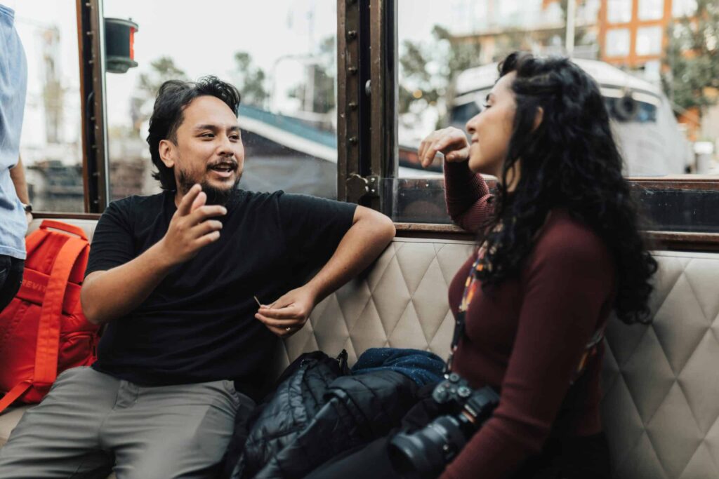 A engaged conversation between two individuals sitting on a boat, surrounded by scenic views outside the windows.
