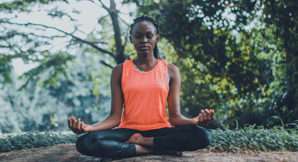 A person sits cross-legged outdoors in a serene environment, practicing meditation amidst lush greenery and soft sunlight.