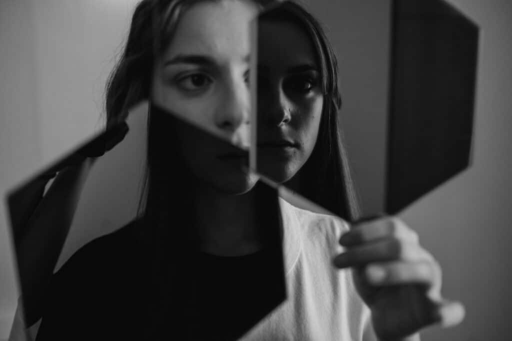 A person holds a fragmented mirror, reflecting their features in a monochromatic setting, creating a sense of introspection.