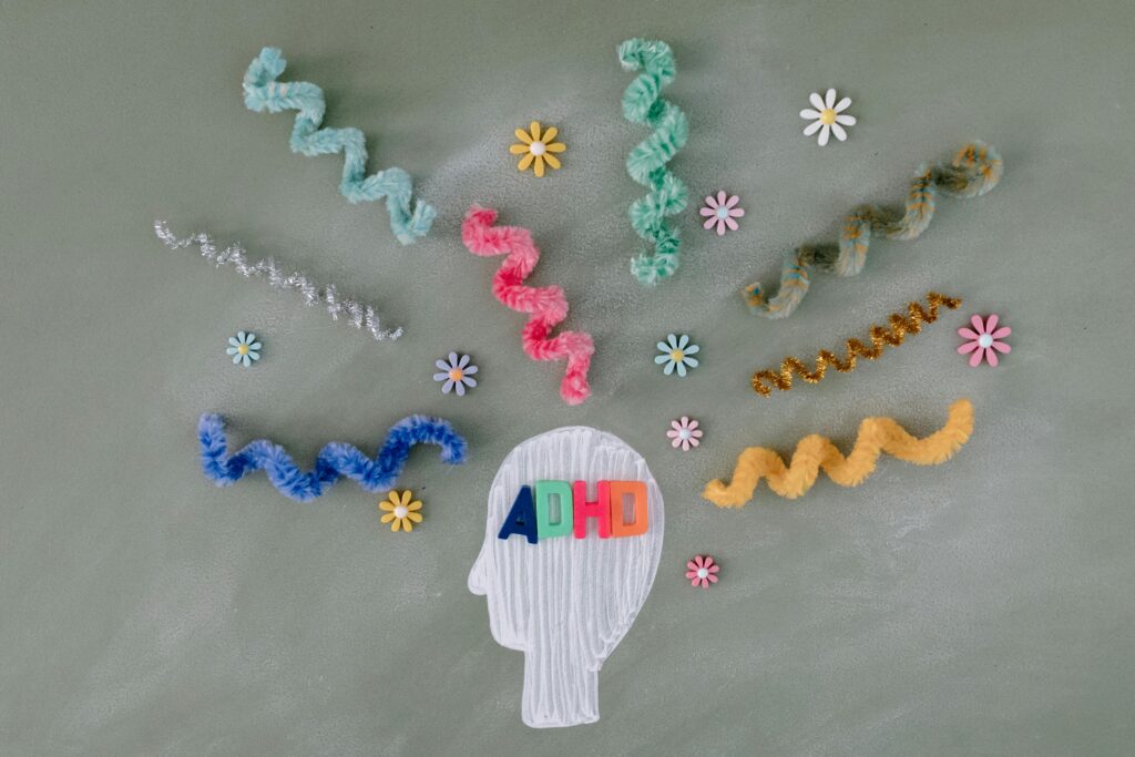 Colorful pipe cleaners and flowers surround a white outline of a head with "ADHD" written across it, symbolizing creative thought.