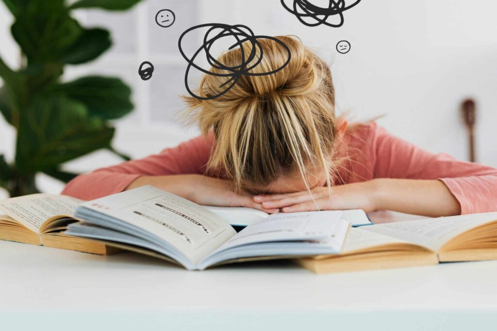 A frustrated girl rests her head on open books, with swirling doodles above her head symbolizing stress and confusion.