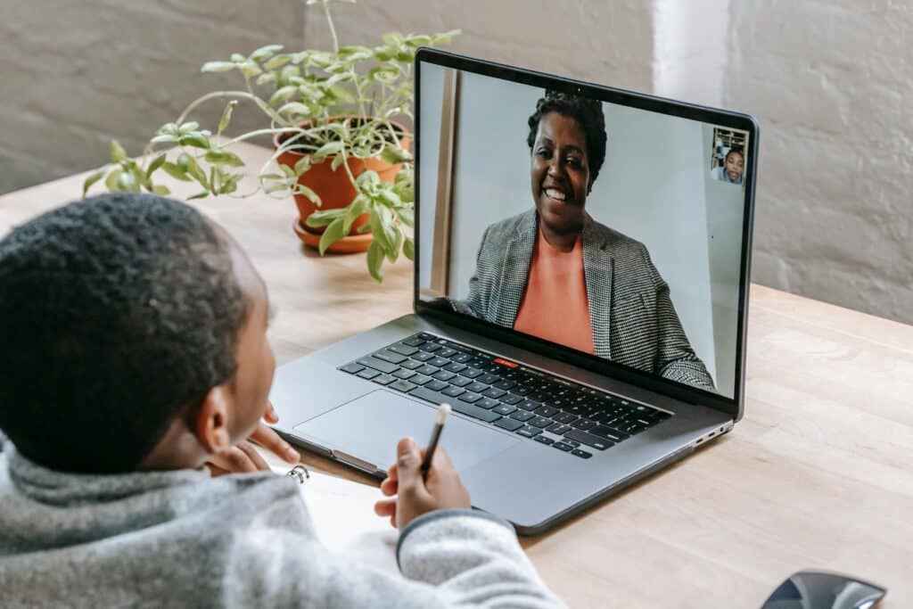 A person sitting at a desk with a laptop, engaged in a virtual meeting with another individual on screen, surrounded by plants.