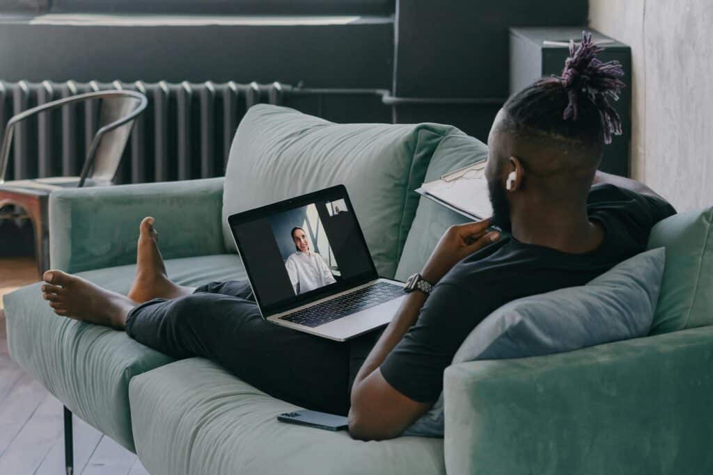 A person lounging on a green sofa, focused on a video call displayed on a laptop in front of them.
