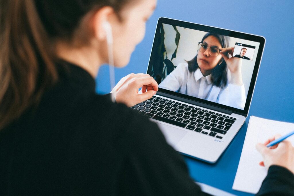 A person participating in a video call on a laptop, with a notebook and pen on the side, engaged in a remote conversation.