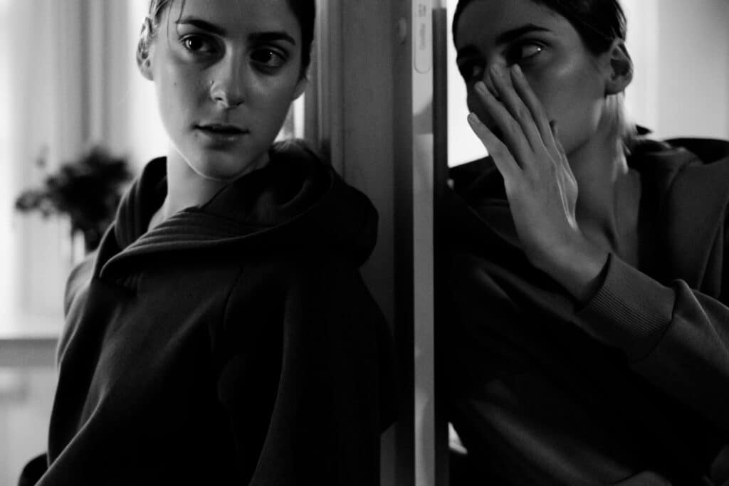 A monochrome image of a person in a hoodie, reflecting in a mirror, creating a sense of introspection and duality.