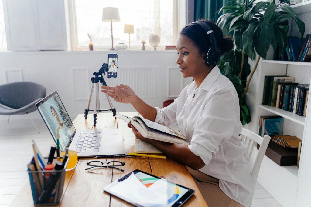 A person in white attire gestures while participating in a video call, surrounded by books and a cozy workspace.