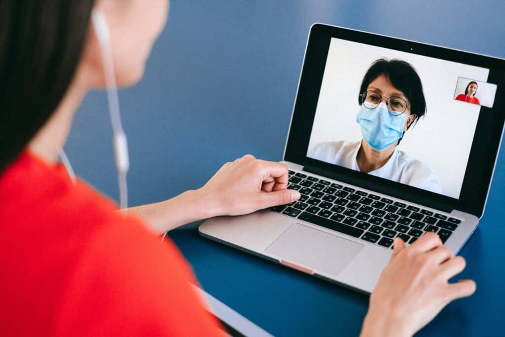 A person in a red shirt participates in a video call using a laptop, engaged in conversation on a blue table surface.
