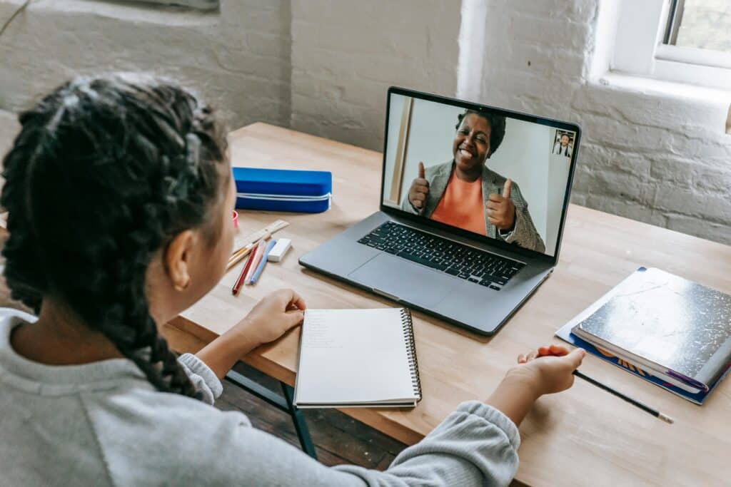 A person sitting at a desk with a notebook and colored pencils, engaged in a video call on a laptop.