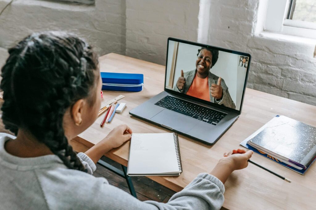 A person sitting at a desk with a notebook and colored pencils, engaged in a video call on a laptop.
