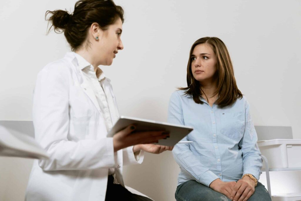 A healthcare professional in a white coat discusses information with a seated patient in a bright, minimalistic office setting.