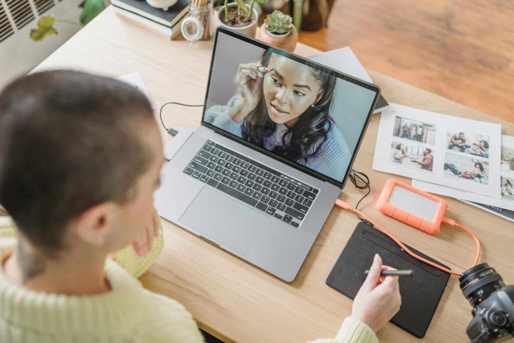 A person in a cream sweater interacts with a laptop during a video call, surrounded by documents and office supplies.