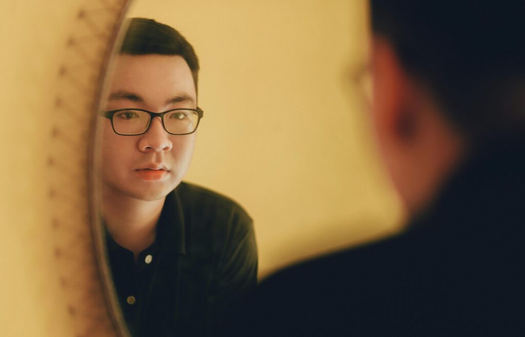 A person gazes into a mirror, reflecting on their thoughts, with warm, soft lighting highlighting the scene.