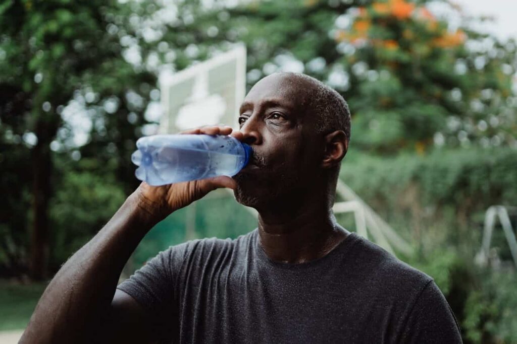 Man drinking water from a bottle outdoors after exercise, representing self-care during recovery.
